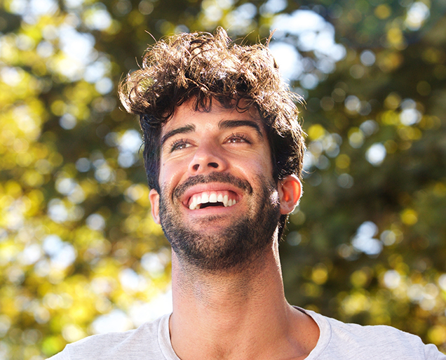 Man with curly dark hair grinning outdoors with durathin veneers in Virginia Beach