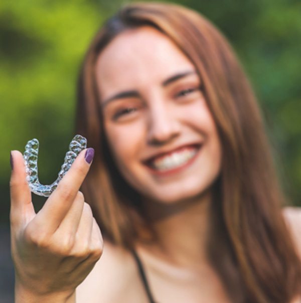 Girl with purple nails outside holding Invisalign smiling