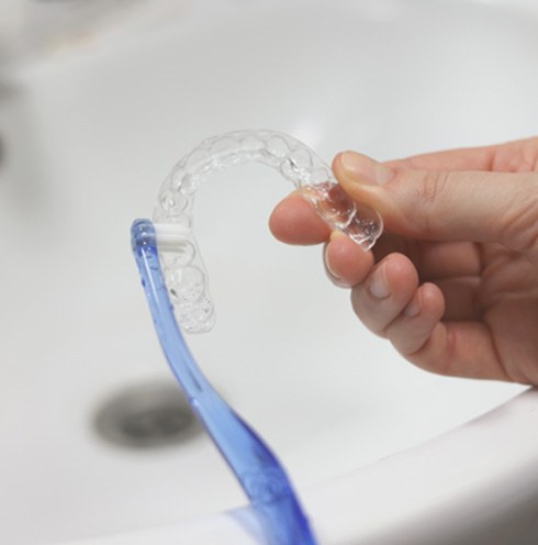 Translucent blue toothbrush scrubbing Invisalign tray over sink