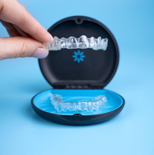 Fingers placing Invisalign into carrying case with light blue background