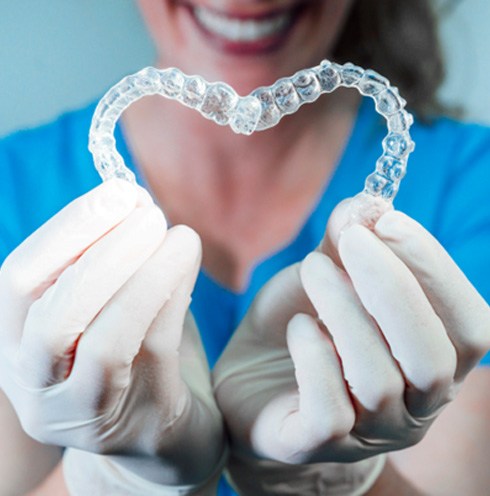 Dentist in blue scrubs holding Invisalign trays in a heart shape
