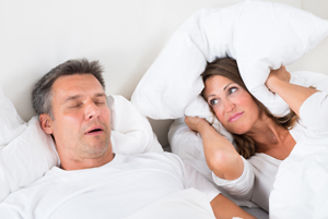 man sleeping while woman covers ears with pillow
